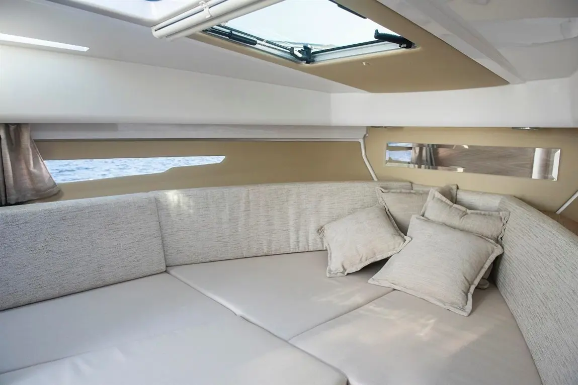 A relaxed interior of a sailboat featuring a cushioned seating area with several decorative pillows and a skylight above.